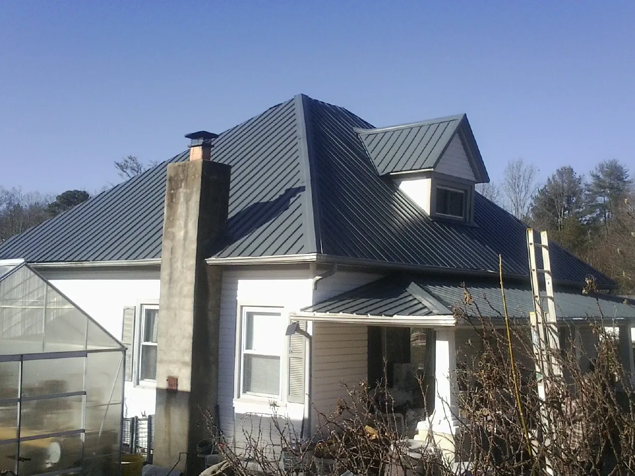Dark blue standing seam metal roof on a white farmhouse with dormer — Slate & Tile Roof Repair by Roofing Brothers in Gate City