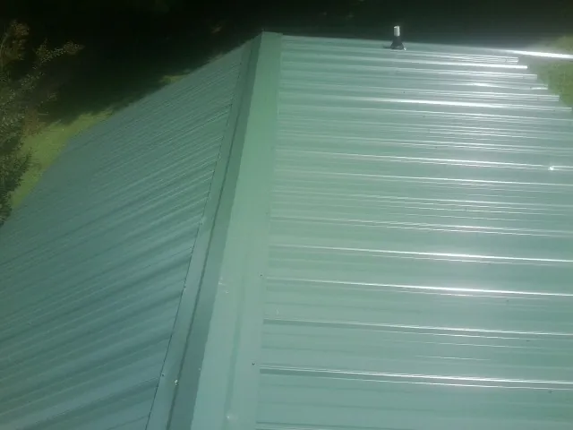 New green metal panels meeting at the ridge of a roof — Flat Roof Repair work by our crew in Gate City