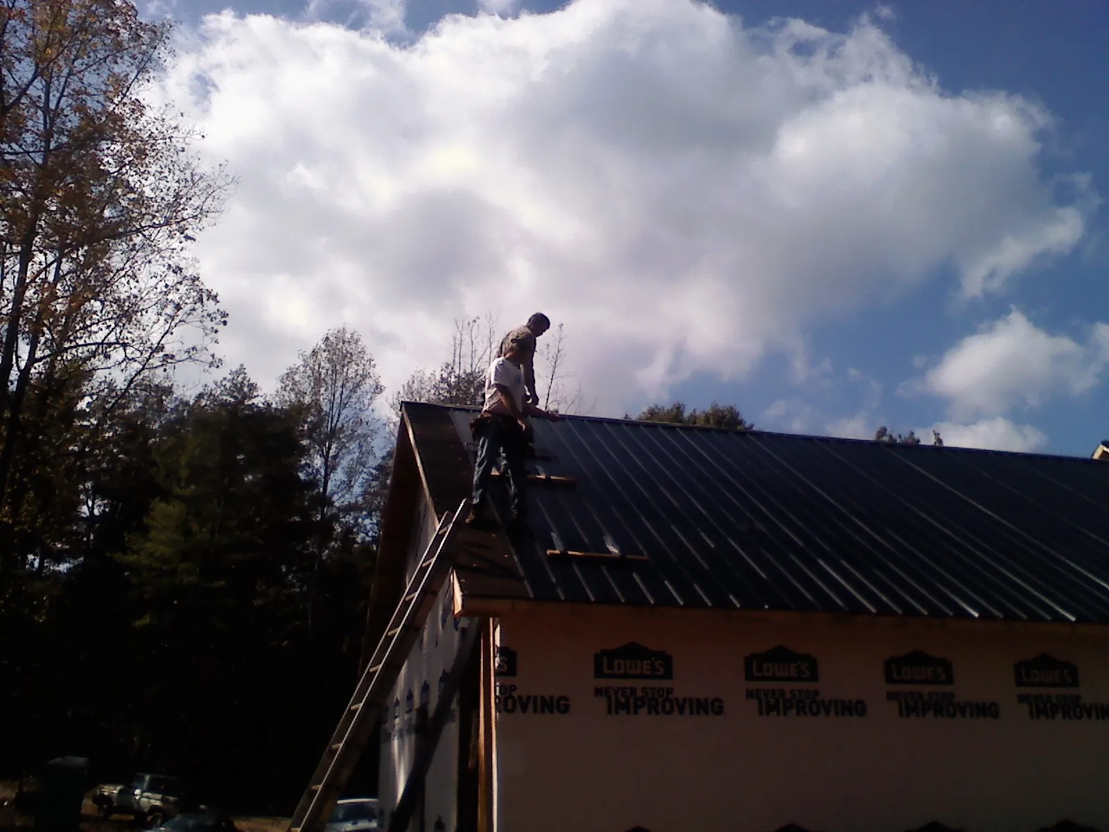 Roofer fastening dark metal panels high against a cloudy sky, from a Roof Inspection job in Gate City