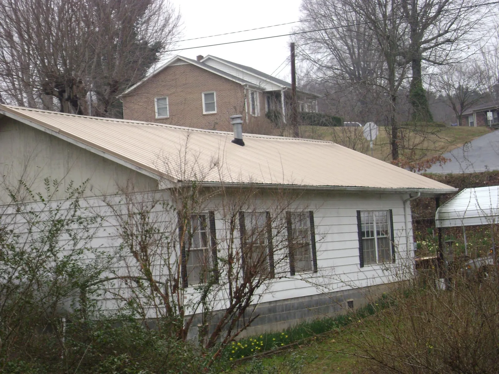 Tan metal roof on a white sided house set into a hillside — Commercial Roofing by Roofing Brothers in Gate City